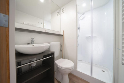 Salle de bains moderne dans Glampingtent avec lavabo, toilettes et douche, design lumineux et épuré.