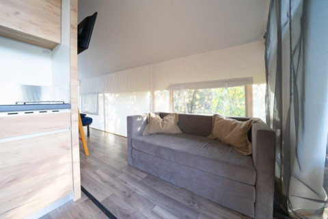 Foto del interior de una tienda glamping safari en De Wije Werelt con sofá, cojines y grandes ventanales.
