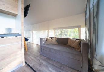 Foto del interior de una tienda glamping safari en De Wije Werelt con sofá, cojines y grandes ventanales.