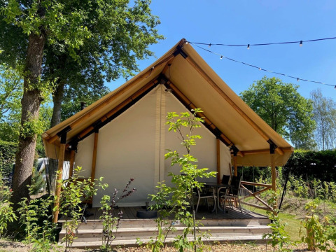 Tente de glamping safari avec terrasse en bois et chaises, entourée de verdure et guirlandes lumineuses.
