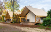 Two safari-style glamping tents with porches in a wooded area at De Wije Werelt in the Netherlands.