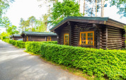 Cabañas de madera rodeadas de setos verdes en el lodge Boekhorst en De Wije Werelt, Países Bajos, día soleado.