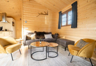 Gezellige woonkamer van lodge Boekhorst op De Wije Werelt in Nederland, met houten muren en comfortabele stoelen.