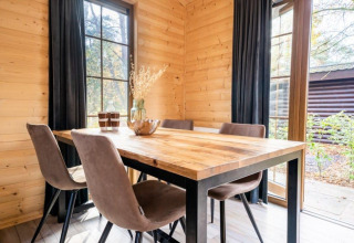 Houten tafel met vier stoelen in lodge Boekhorst bij De Wije Werelt, Nederland, met zicht op het groen buiten.