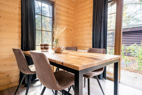 Houten tafel met vier stoelen in lodge Boekhorst bij De Wije Werelt, Nederland, met zicht op het groen buiten.