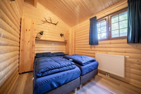 Houten slaapkamer in Boekhorst-lodge, De Wije Werelt, Nederland, met twee eenpersoonsbedden en blauw beddengoed.