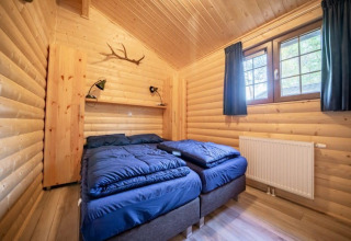 Houten slaapkamer in de Boekhorst lodge, De Wije Werelt, Nederland, met twee bedden en blauwe dekbedden.