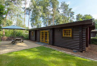 Buitenaanzicht van een houten lodge Boekhorst op De Wije Werelt in Nederland met terras en parasol.