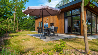 Udendørs opholdsområde ved Pavilion-lodgen på De Wije Werelt i Holland, med mennesker og parasol.