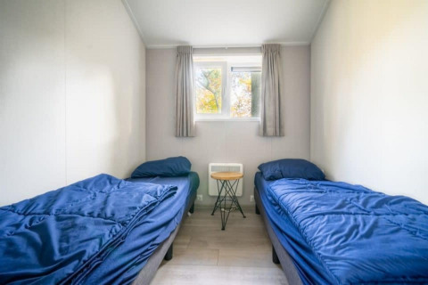 Chambre avec deux lits simples, draps bleus, petite table et fenêtre à la Berkel lodge, De Wije Werelt, Pays-Bas.