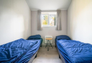 Dormitorio con dos camas individuales, ropa de cama azul, mesita y ventana en Berkel lodge, De Wije Werelt, Países Bajos.