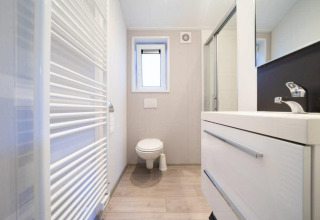 Baño moderno en la cabaña Berkel de De Wije Werelt, Países Bajos, con inodoro, lavabo y ducha iluminada.
