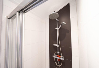Ducha en baño moderno de Berkel, alojamiento De Wije Werelt, con puerta de vidrio y pared oscura, Países Bajos.