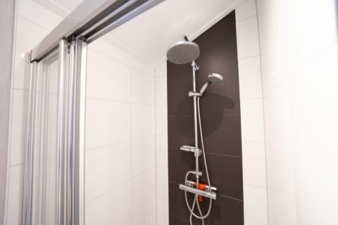 Ducha en baño moderno de Berkel, alojamiento De Wije Werelt, con puerta de vidrio y pared oscura, Países Bajos.