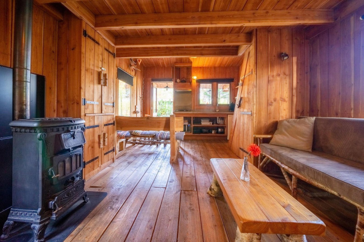 Interior de madera de Nature Lodge en De Wije Werelt, Países Bajos, con estufa y muebles rústicos.