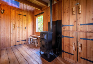 Interior revestido de madera con estufa, armarios y ventana en Nature Lodge en De Wije Werelt, Países Bajos.