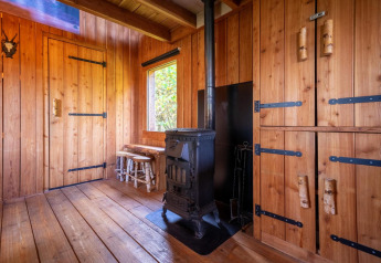 Interior revestido de madera con estufa, armarios y ventana en Nature Lodge en De Wije Werelt, Países Bajos.