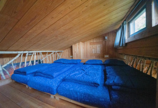 Dachzimmer der Nature Lodge bei De Wije Werelt in den Niederlanden mit Holzwänden und blauen Betten.