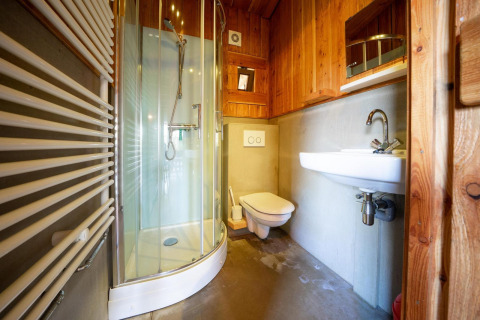 Moderne badeværelse med buet brusekabine, væghængt toilet og håndvask i træbeklædt Nature Lodge.