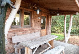 Cabaña de madera con banco y mesa rústicos en el porche en Nature Lodge de De Wije Werelt, Países Bajos.