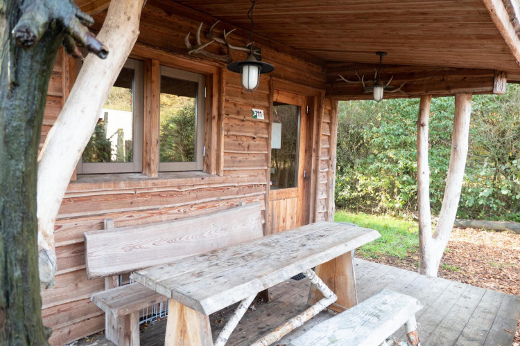 Cabaña de madera con banco y mesa rústicos en el porche en Nature Lodge de De Wije Werelt, Países Bajos.