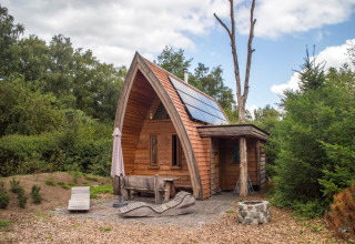 Kleine houten tiny house met zonnepanelen en gebogen dak bij De Wije Werelt, Nederland.