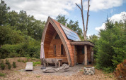 Pequeña casa de madera con paneles solares y techo curvado rodeada de naturaleza en De Wije Werelt, Países Bajos.