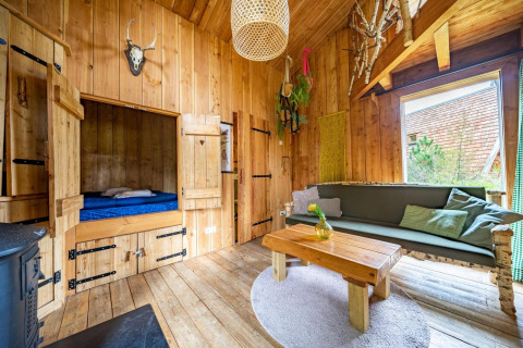 Intérieur chaleureux en bois d'une Nature Lodge à De Wije Werelt, Pays-Bas, avec canapé et alcôve.