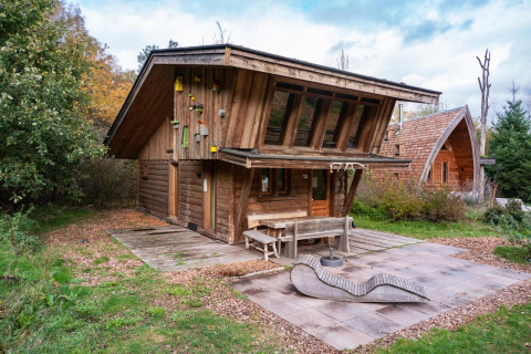 Houten huisje bij Nature Lodge op De Wije Werelt in Nederland, omgeven door bomen en buitenzitje.
