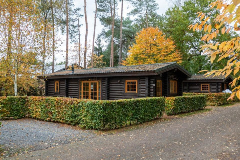 Accogliente baita in legno al Boekhorst Lodge, tra alberi autunnali e siepi curate verdi.
