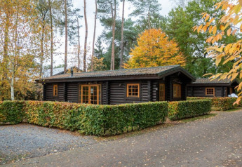 A cozy dark wood cabin at Boekhorst Lodge, surrounded by autumn trees and neat green hedges.