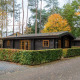 En hyggelig træhytte ved Boekhorst Lodge, omgivet af træer med efterårsblade og grønne hække.