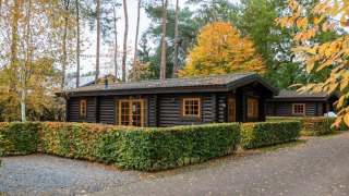 Chalet en bois Boekhorst Lodge entouré d’arbres colorés d’automne et de haies bien taillées.