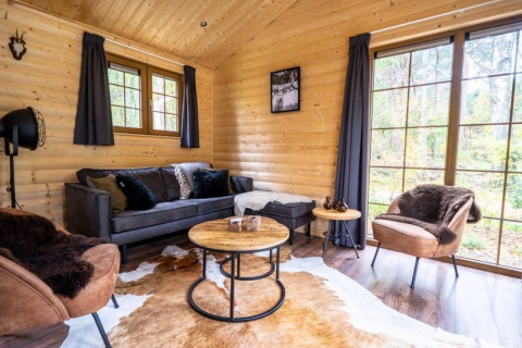 Knusse woonkamer in lodge Boekhorst, De Wije Werelt, Nederland, met houten wanden en ruime raampartijen.