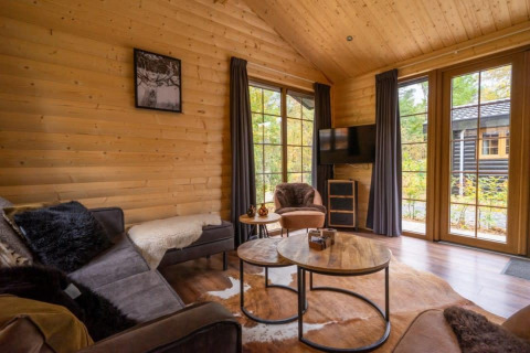 Salon chaleureux d’un lodge en bois avec grandes fenêtres et vue nature à Boekhorst, De Wije Werelt, Pays-Bas.