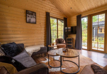 Salon chaleureux d’un lodge en bois avec grandes fenêtres et vue nature à Boekhorst, De Wije Werelt, Pays-Bas.