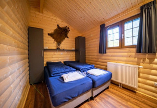 Dormitorio en Boekhorst lodge en De Wije Werelt, Países Bajos, paredes de madera y dos camas azules.