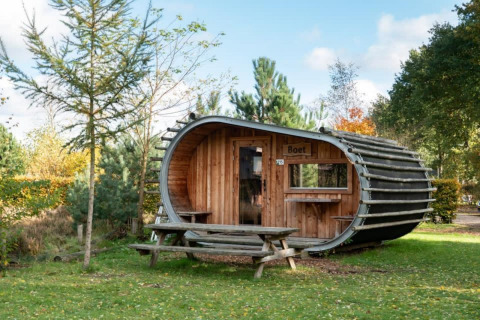 Une mini-maison en forme de tonneau nommée Boet, dans la nature, entourée d’arbres et d’une table de pique-nique.
