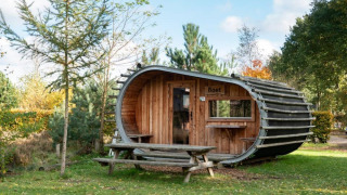 Une mini-maison en forme de tonneau nommée Boet, dans la nature, entourée d’arbres et d’une table de pique-nique.