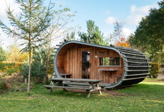 Une mini-maison en forme de tonneau nommée Boet, dans la nature, entourée d’arbres et d’une table de pique-nique.