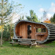 En unik, tøndeformet tiny house ved navn Boet i naturen, omgivet af træer og et picnicbord foran.