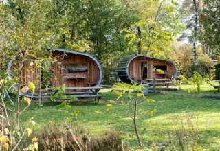 Dos pequeñas casas ovaladas de madera llamadas Boet en De Wije Werelt, Países Bajos, rodeadas de naturaleza verde.