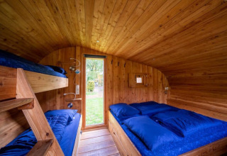 Interior de una tiny house Boet en De Wije Werelt, Países Bajos, con paneles de madera y ropa de cama azul.