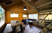 Indvendig udsigt over Glampingtent på De Wije Werelt i Holland med træborde, sofa og tekøkken.