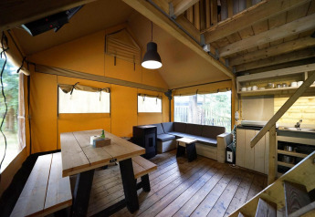 Indvendig udsigt over Glampingtent på De Wije Werelt i Holland med træborde, sofa og tekøkken.