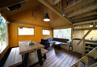 Vista interior de una tienda Glampingtent en De Wije Werelt, Países Bajos, con muebles de madera y sofá.