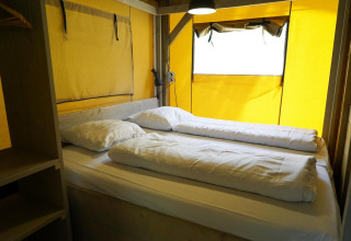 Interior de una tienda safari glamping con cama doble y paredes amarillas en De Wije Werelt, Países Bajos.