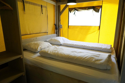 Interior de una tienda safari glamping con cama doble y paredes amarillas en De Wije Werelt, Países Bajos.