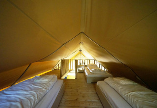 Vista interior de una tienda safari glamping con tres camas individuales en De Wije Werelt, Países Bajos.