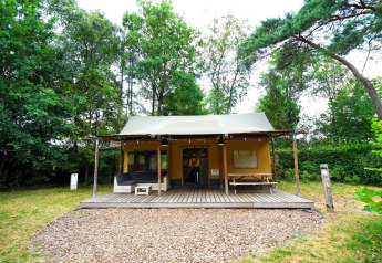 Tente safari glamping à De Wije Werelt aux Pays-Bas, entourée d’arbres et terrasse en bois devant.